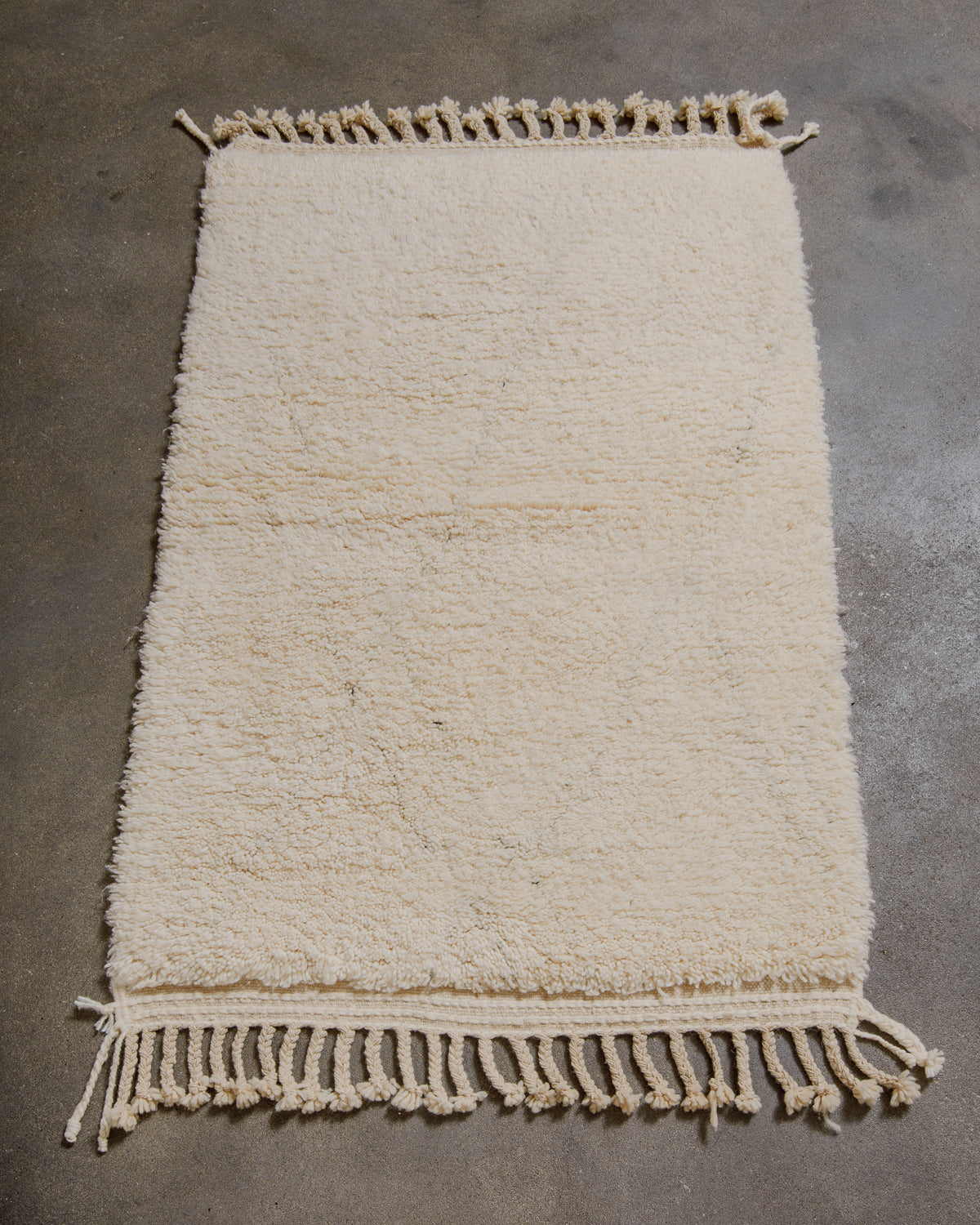 Cream woven rug with tassels on a gray concrete floor